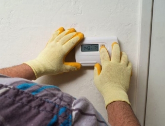 HVAC professional wearing yellow gloves inspecting thermostat