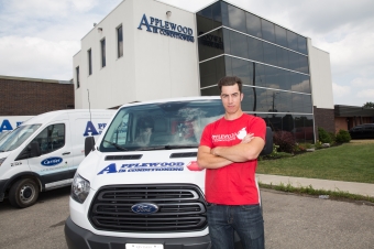Applewood air conditioning employee wearing a red shirt standing in front of company building and van